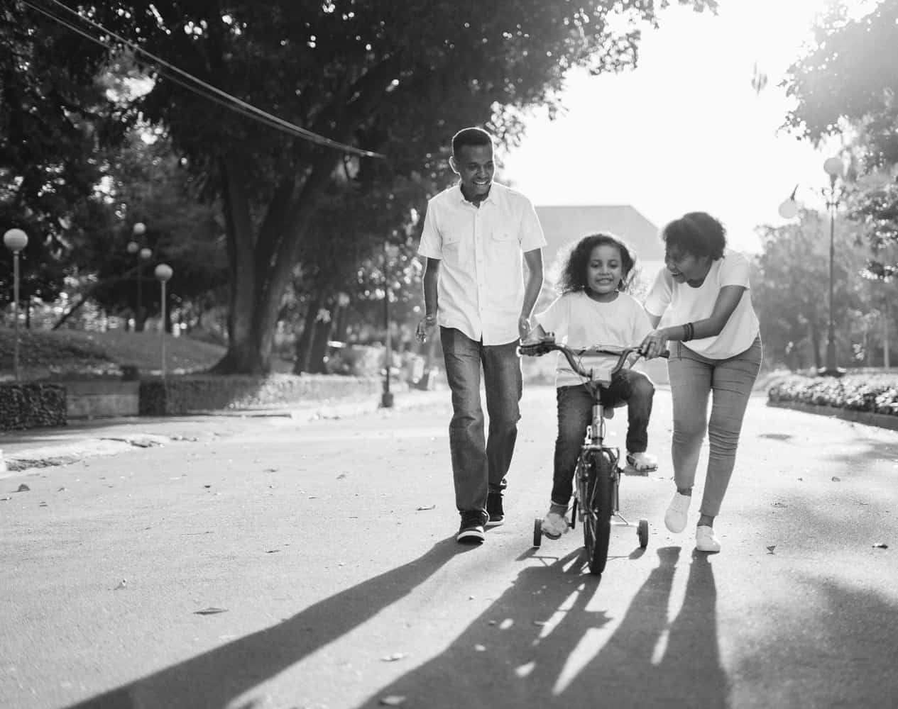 family, with mom and dad teaching child to ride a bike