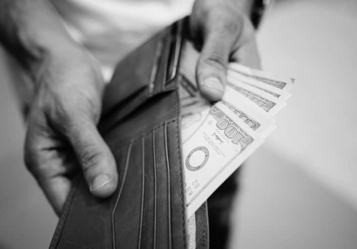 image of a man holding a wallet and pulling out 100 dollar bills