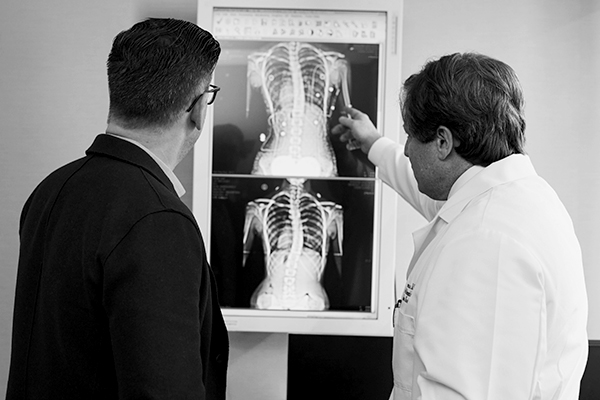 Doctor pointing at a x-ray result next to a man wearing a black suit.